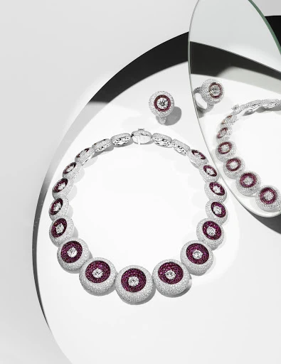 Elegant jewelry shot: A silver necklace and ring with ruby and diamond accents are displayed on a white surface with mirror reflections.