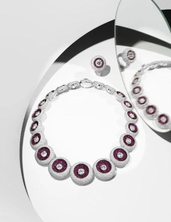 Elegant jewelry shot: A silver necklace and ring with ruby and diamond accents are displayed on a white surface with mirror reflections.