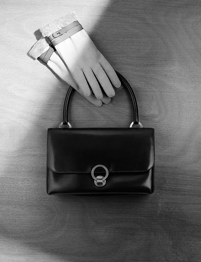 Black leather handbag and leather gloves on a wooden surface captured in a top-down still life by Philippe Lacombe.