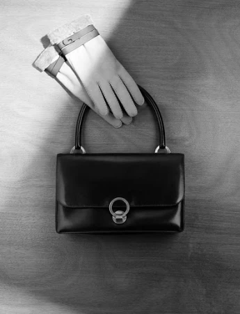 Black leather handbag and leather gloves on a wooden surface captured in a top-down still life by Philippe Lacombe.
