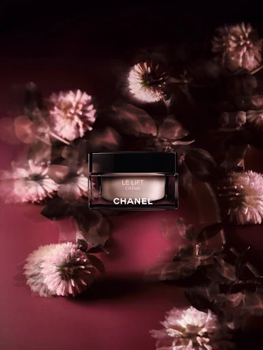 Cream jar by Chanel with LE LIFT Crème label and flowers in pink-toned light. Beauty product photography in studio setting.