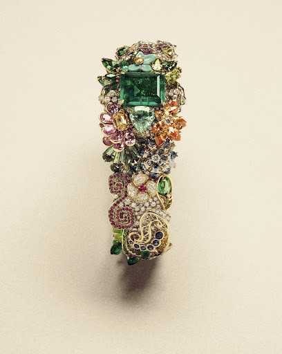 Close-up of a gemstone bracelet featuring a large square-cut emerald as the central stone, surrounded by other colorful gems and metalwork.