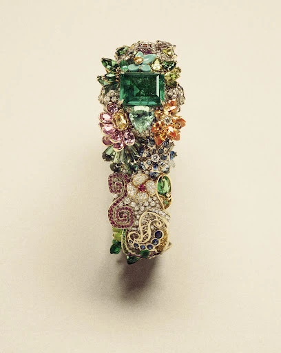Close-up of a gemstone bracelet featuring a large square-cut emerald as the central stone, surrounded by other colorful gems and metalwork.