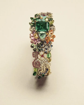 Close-up of a gemstone bracelet featuring a large square-cut emerald as the central stone, surrounded by other colorful gems and metalwork.