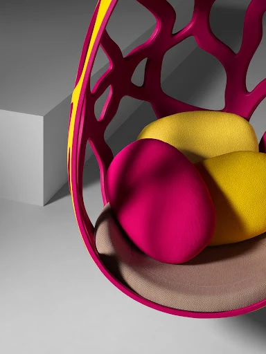 Vibrant pink and yellow egg chair with patterned cutouts and soft cushions, casting shadows against a gray backdrop in a photo studio.