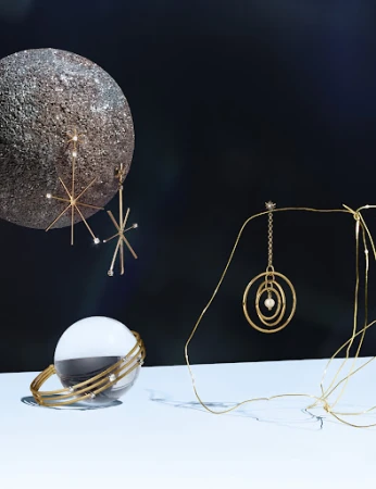 Still life shot of gold jewelry, including starburst earrings, a bangle bracelet, and a circular pendant, against a dark background.