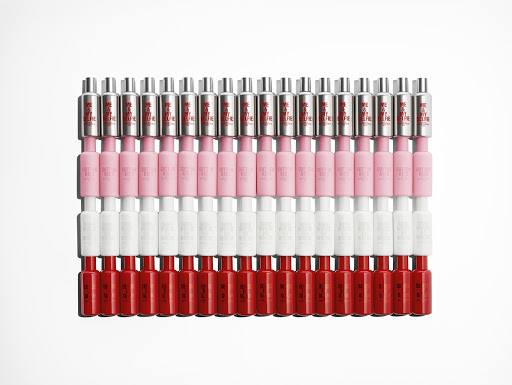 Rows of red, white, pink and silver bottles displayed on a white surface, arranged in neat rows forming a rectangular block.
