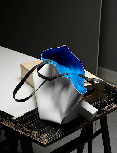 Fashionable tote bag with black straps, featuring a white exterior and a bright blue interior, sits on a rustic wooden table.