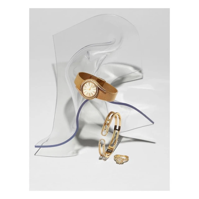 Elegant gold wristwatch, bracelet, and ring displayed on clear acrylic risers against a clean white backdrop in a studio setting.
