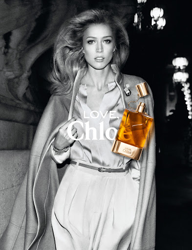 Black and white fashion advertisement featuring a blonde woman in a coat, blouse, and pants with a bottle of Chloe perfume.
