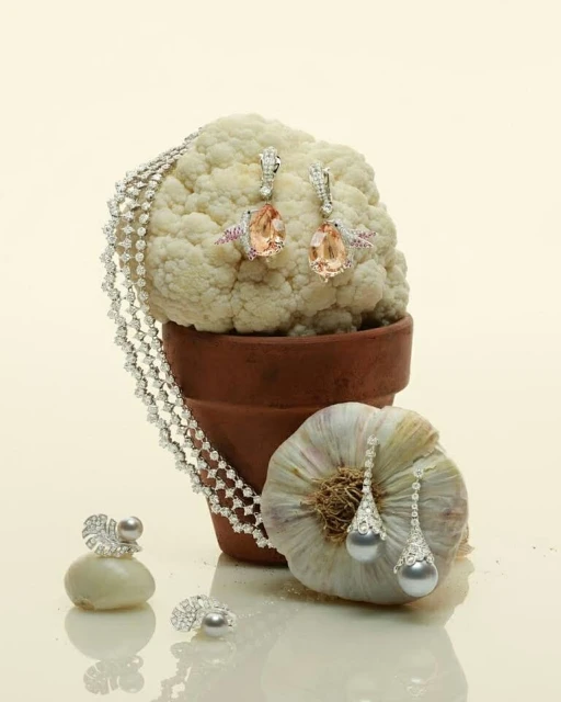 Elegant jewelry still life featuring a diamond necklace, earrings, and rings creatively arranged with fresh cauliflower and garlic.