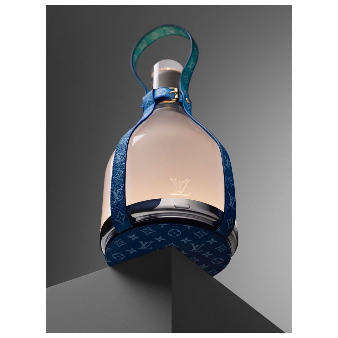 Elevated view of a Louis Vuitton lantern-style object featuring blue patterned leather straps and a glowing center, presented on a gray surface.