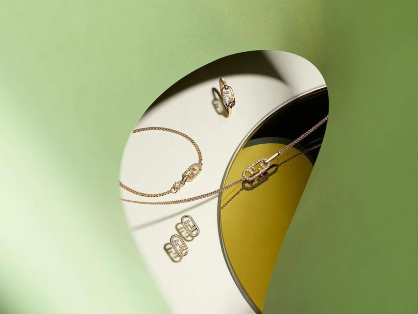 Still life of gold jewelry including necklace, ring, and earrings arranged on a two-tone background bisected by a curved paper cutout.