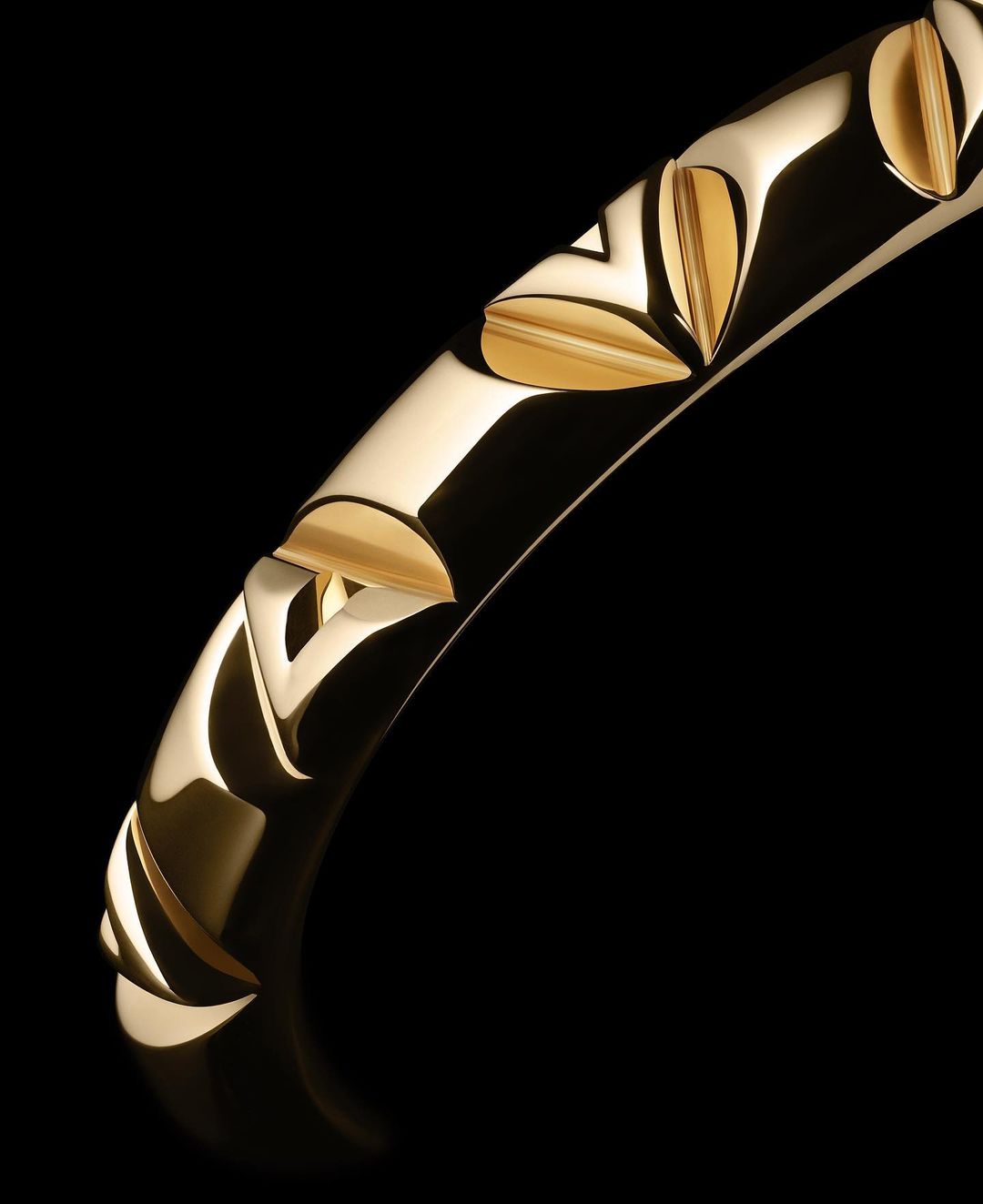 Close-up of a gold bangle bracelet featuring geometric cut-out details, isolated against a black background to accentuate its design and shine.
