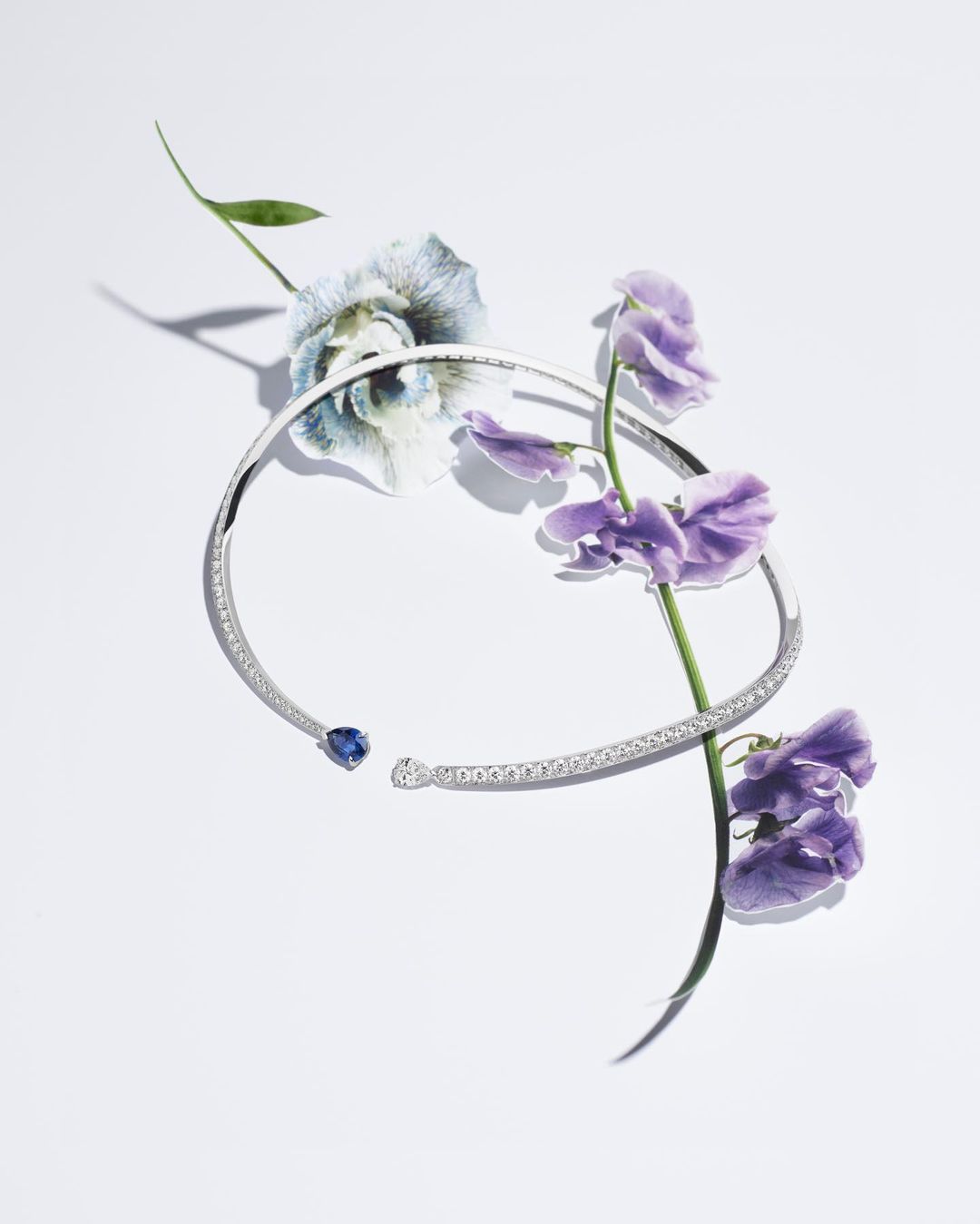 Necklace with a blue gemstone and purple flowers creates an elegant composition on a white backdrop, showcasing jewelry and nature.