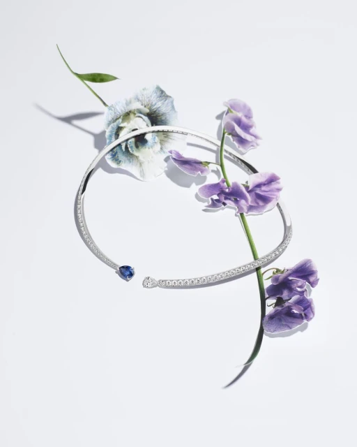 Necklace with a blue gemstone and purple flowers creates an elegant composition on a white backdrop, showcasing jewelry and nature.