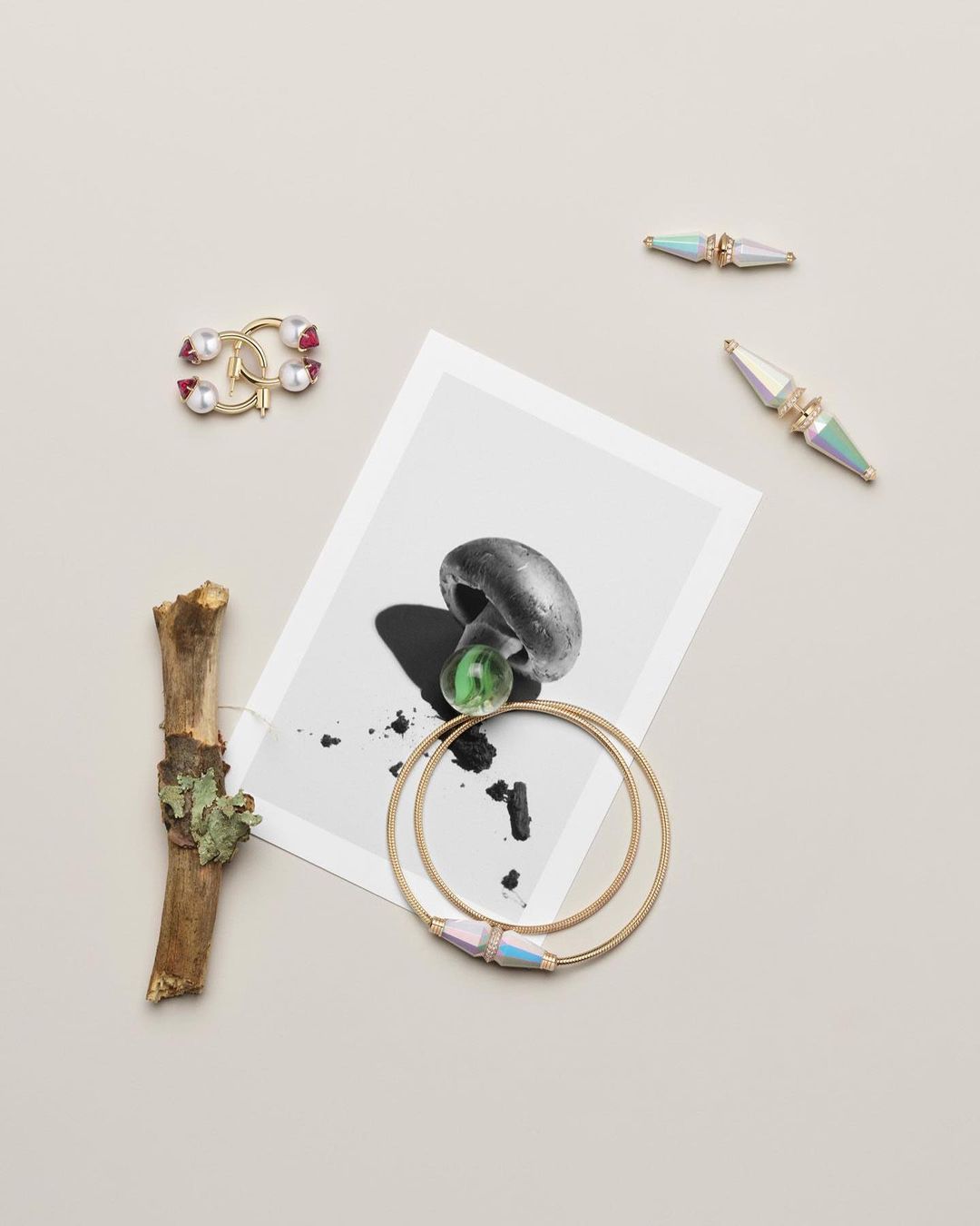 Flat lay of a mushroom photo, twig, and gold jewelry on a light surface creating a minimalist and aesthetic product display.