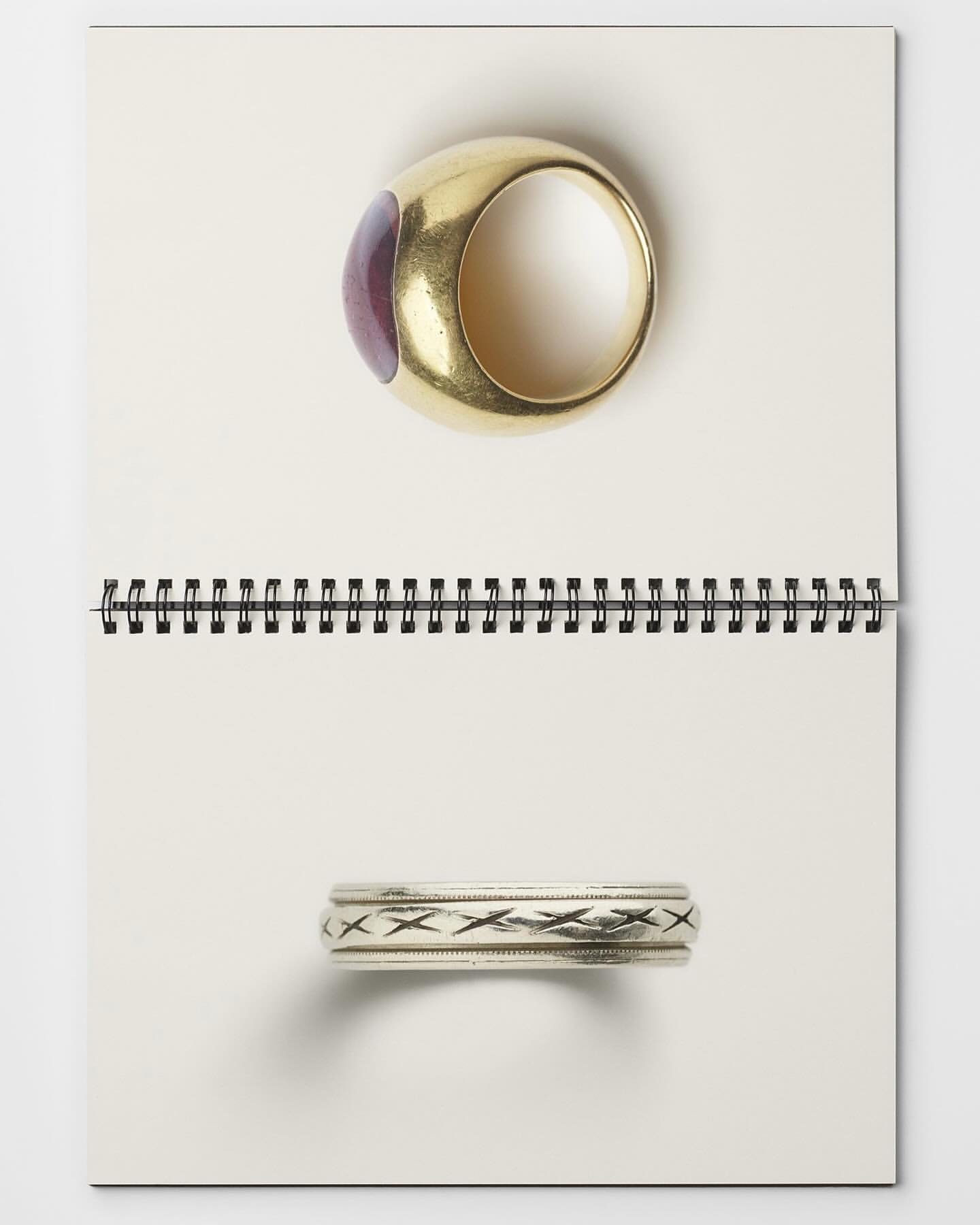 Two rings, one gold with a purple stone and one silver with a decorative band, sit on a white spiral-bound notebook.