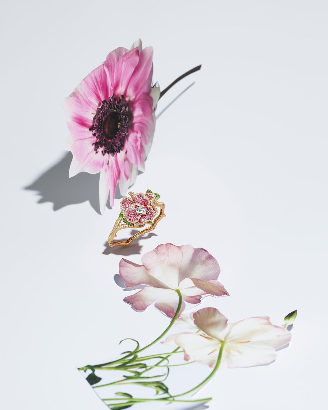 Floral-themed jewellery shot featuring a ring with a floral design, pink petals, and a white background under bright studio lighting.