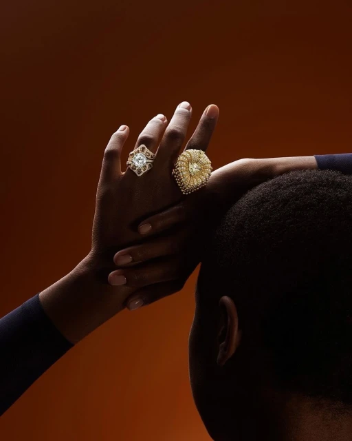 Close-up of an adult hand adorned with two gold decorative rings against a warm brown background with side lighting.