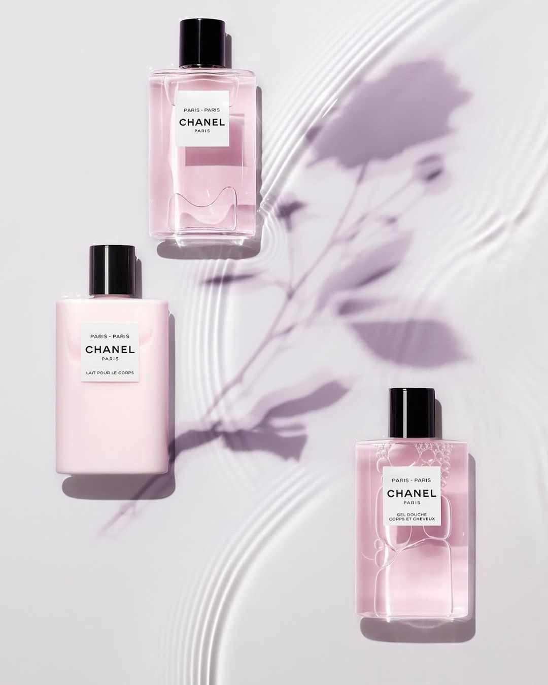 Three bottles of Chanel Paris-Paris fragrance are arranged on a pale background, casting a soft shadow, accentuating their elegant design.