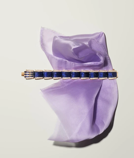 Elegant bracelet on a draped purple silk scarf against a white background, showcasing jewelry and fabric textures in a studio setting.