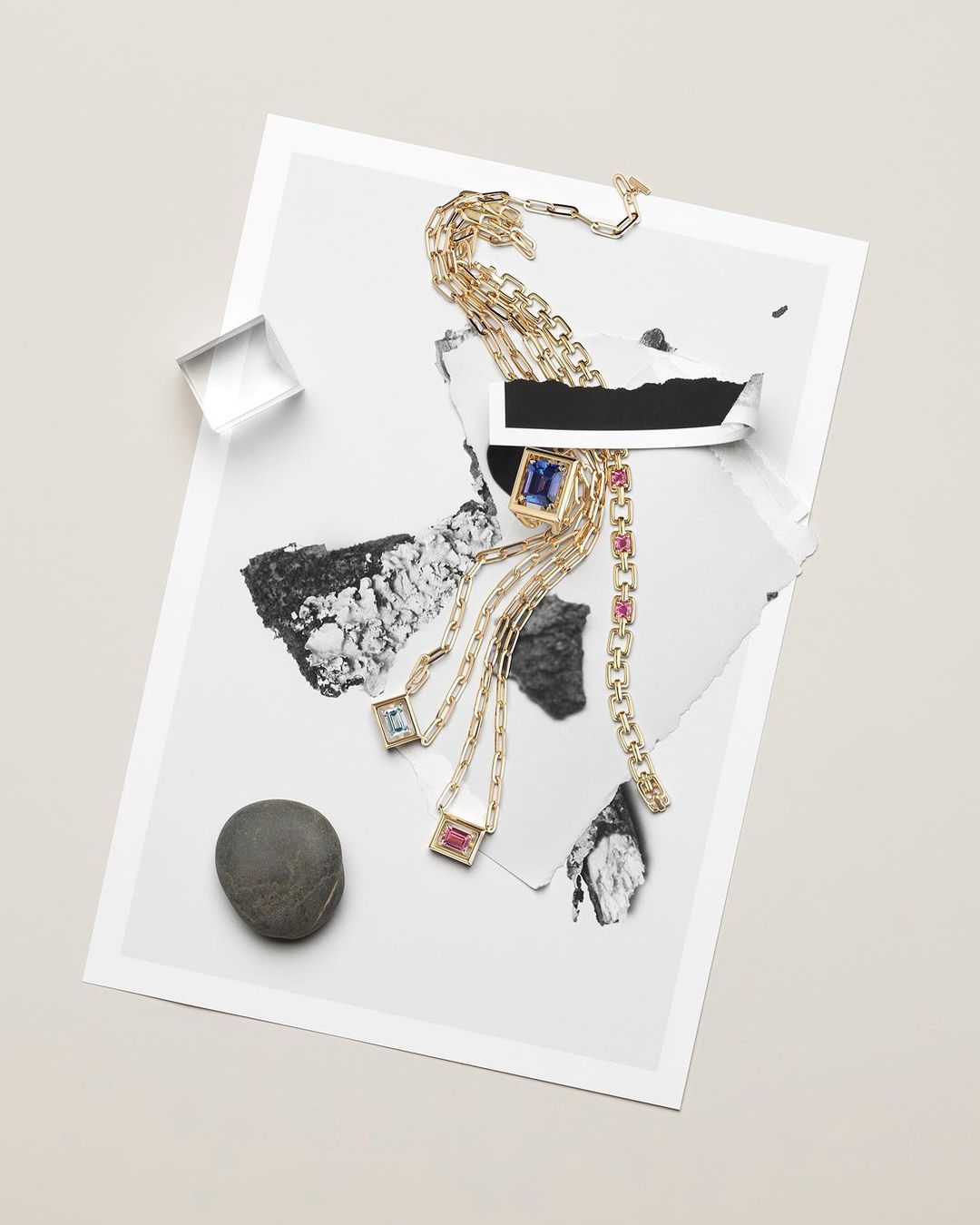 Still life shot of gold jewelry, including necklaces and a bracelet with gemstones, arranged on top of a piece of torn paper.