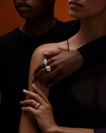 Close-up portrait of two people wearing diamond rings on their fingers, photographed by Philippe Lacombe against a warm background.