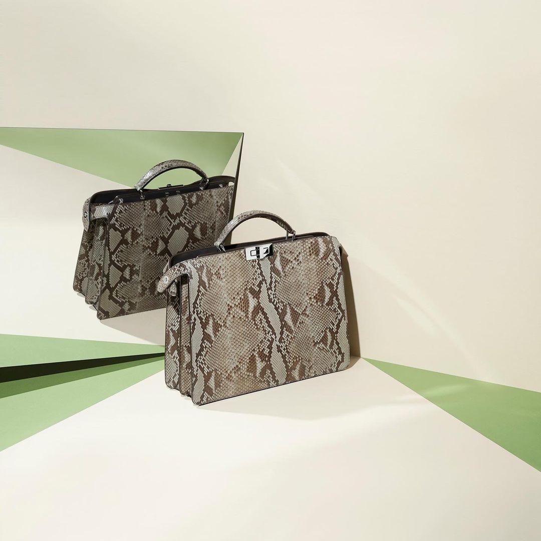 Fashion shot of a beige snakeskin-patterned handbag positioned next to its reflection, against a backdrop with light green accents.