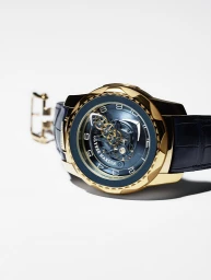 Close-up product photograph of a luxury gold wristwatch with a blue dial and leather strap on a white background.