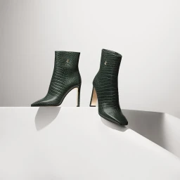 Two dark green crocodile-embossed leather boots with high heels displayed on a white studio platform.