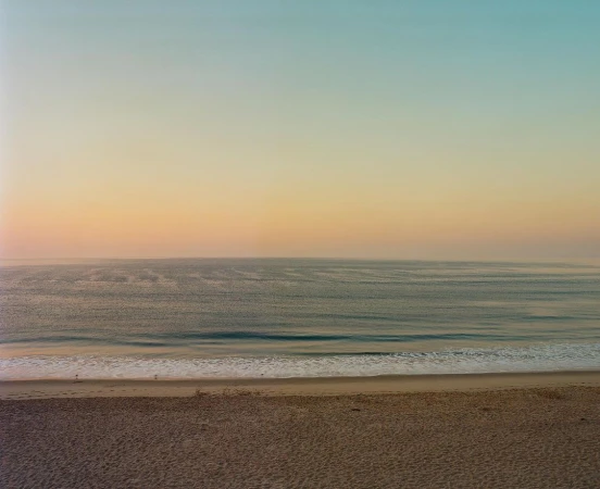 Serene coastal landscape featuring a sandy beach, calm ocean waves, and a gradient sunset sky captured by Rainer Hosch.
