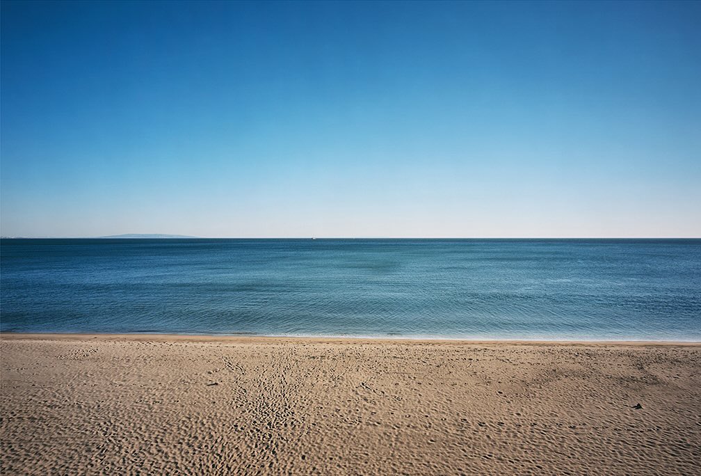 Scenic beach landscape featuring sandy shore meeting calm blue ocean under a clear sky, evoking tranquility and natural beauty.