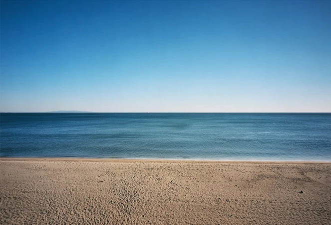 Scenic beach landscape featuring sandy shore meeting calm blue ocean under a clear sky, evoking tranquility and natural beauty.