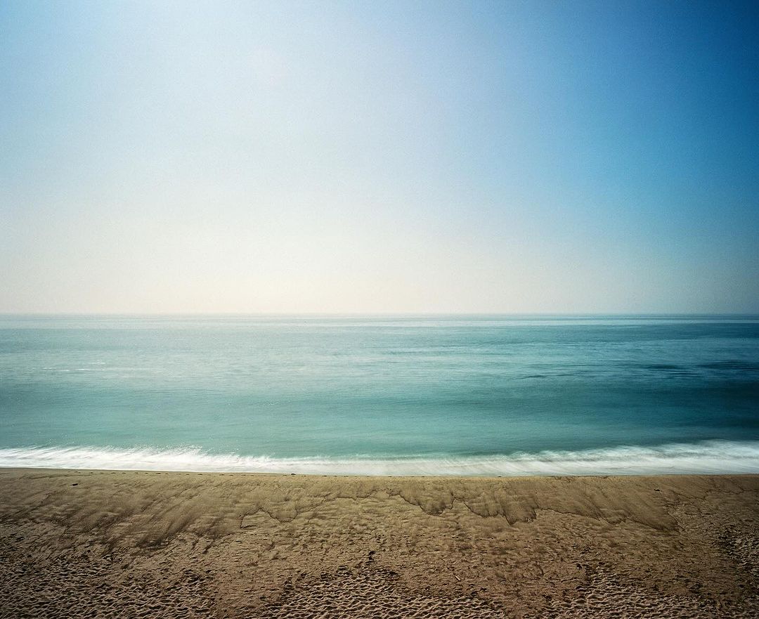 Scenic view of calm ocean waves meeting sandy beach under a clear sky, creating a serene coastal landscape with a sense of tranquility.
