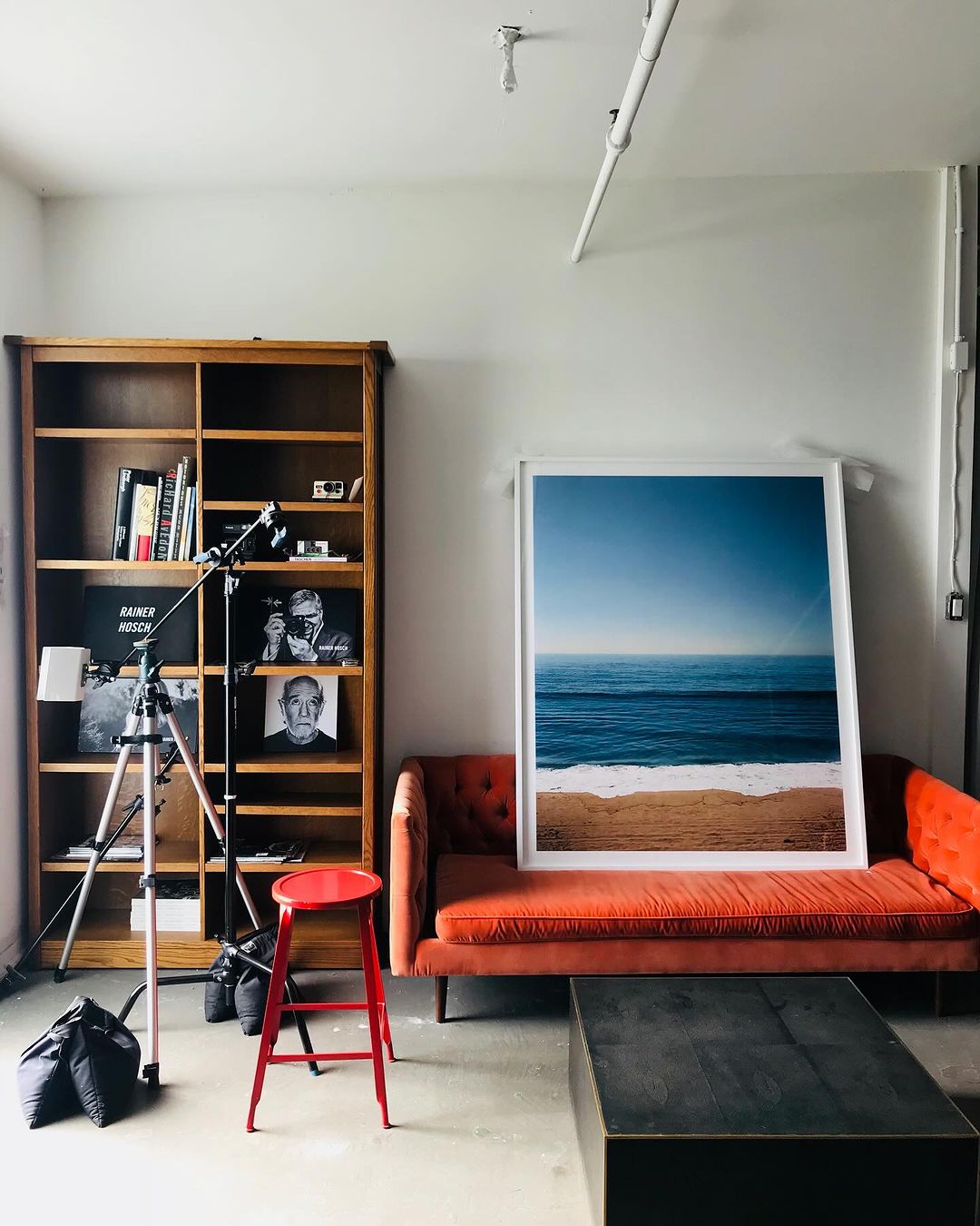 Living room interior with a bright orange couch, dark wood coffee table, and a framed ocean photograph leaning on the sofa.