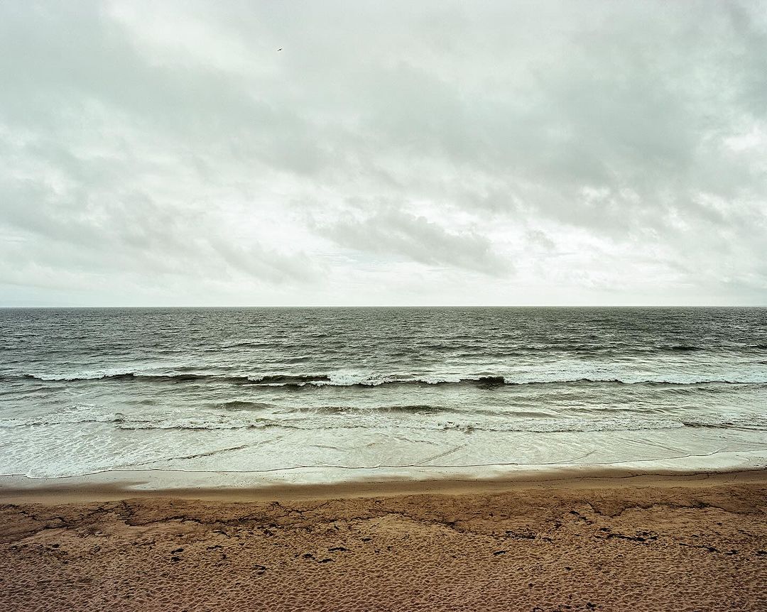 Scenic beach view featuring the ocean's waves meeting the sandy shore under a cloudy sky. Tranquil seascape with natural beauty.