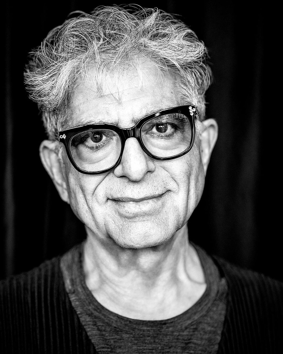 Portrait of an elderly man with glasses and textured hair against a dark backdrop by Rainer Hosch.