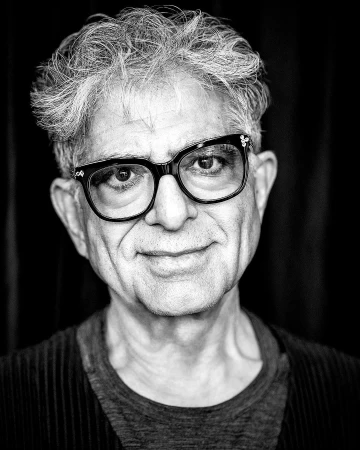 Portrait of an elderly man with glasses and textured hair against a dark backdrop by Rainer Hosch.