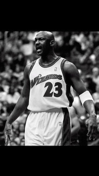 Black-and-white medium shot of basketball player Michael Jordan in a Wizards jersey, with a crowd visible in the background.