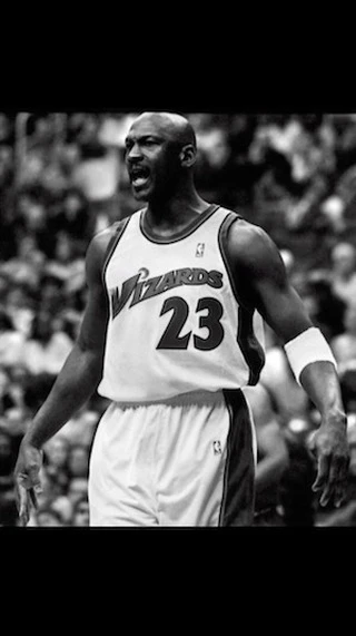 Black-and-white medium shot of basketball player Michael Jordan in a Wizards jersey, with a crowd visible in the background.