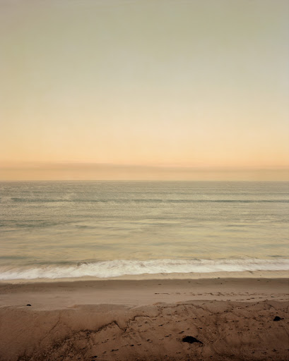 Scenic beach landscape featuring a sandy shore meeting a calm ocean under a gradient sky with muted earth tones.