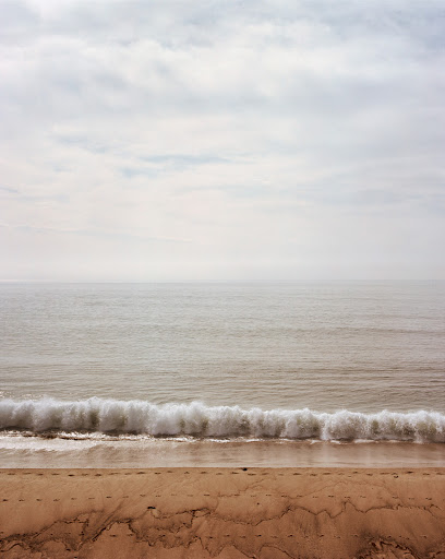 Minimalist seascape featuring a sandy beach, foamy waves, and a cloudy sky. Serene ocean scene with natural colors and soft lighting.