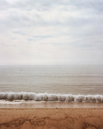 Minimalist seascape featuring a sandy beach, foamy waves, and a cloudy sky. Serene ocean scene with natural colors and soft lighting.