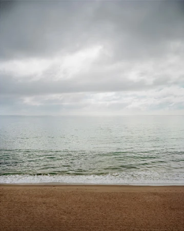 Calm ocean waves meeting a sandy beach under an overcast cloudy sky captured in a vertical frame.