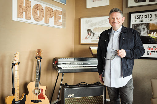 Man stands in music room with guitars, keyboard, amp, and framed posters creating a stylish and creative atmosphere.