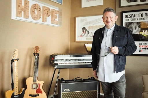 Man stands in music room with guitars, keyboard, amp, and framed posters creating a stylish and creative atmosphere.