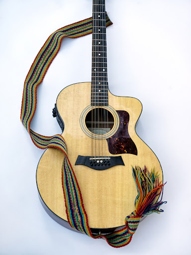 Acoustic guitar with a colorful woven strap, presented against a bright white background in a visually appealing studio shot.