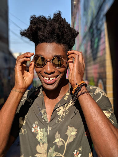 Portrait of smiling Black man with afro wearing round sunglasses and floral shirt in urban setting, good lighting, clear face, cool