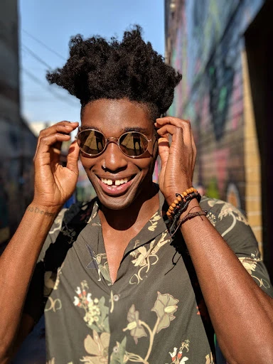 Portrait of smiling Black man with afro wearing round sunglasses and floral shirt in urban setting, good lighting, clear face, cool